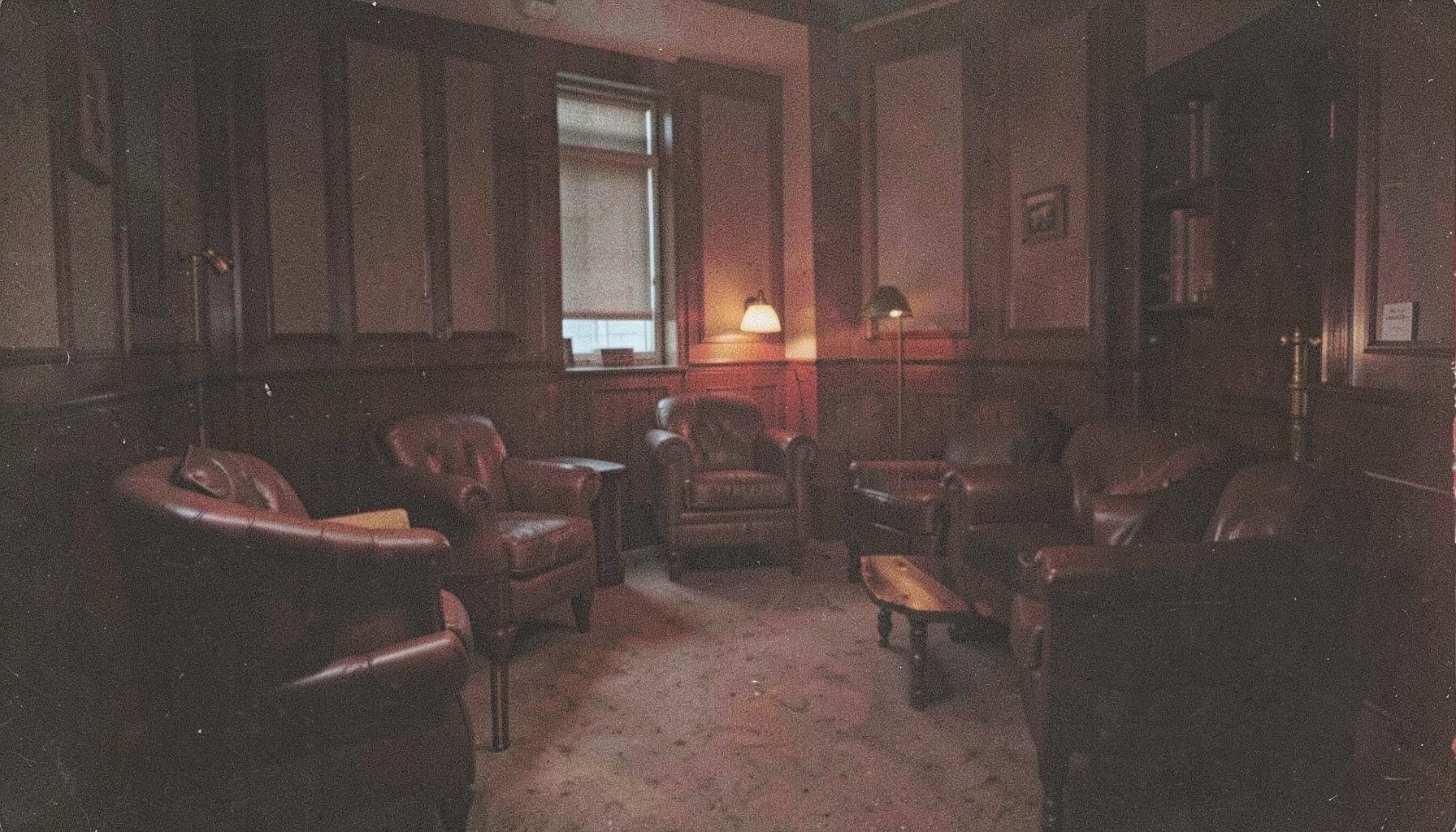 Dark grainy photograph of an empty barristers' common room with leather armchairs and low lamplight, quiet and contemplative atmosphere