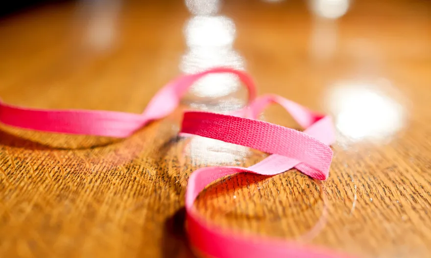 A softly lit close-up of a pink ribbon resting on polished dark wood, warm amber tones blending into deep shadow, evoking quiet reflection and personal resolve.